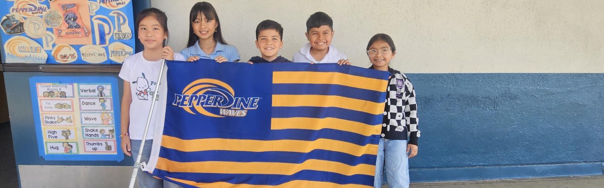 Children holding a Pepperdine flag in front of a school wall.