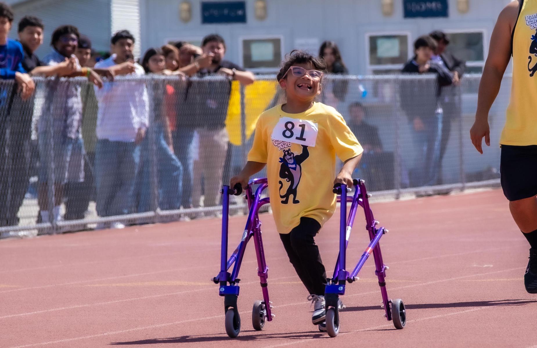 young student athlete competes while using walker and is cheered buy older students