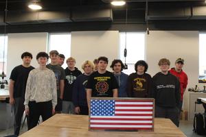 tech ed students standing around wooden flag they created