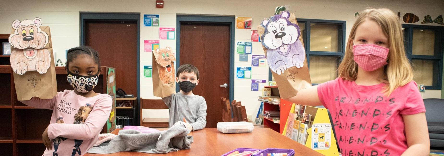 3 students holding up the paper sack puppets they made