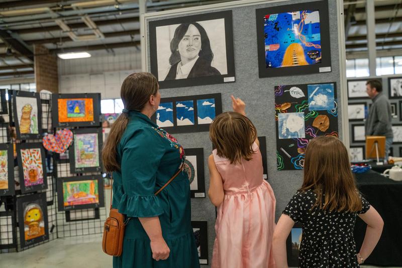 a parent and two students looking at art work at the district art show