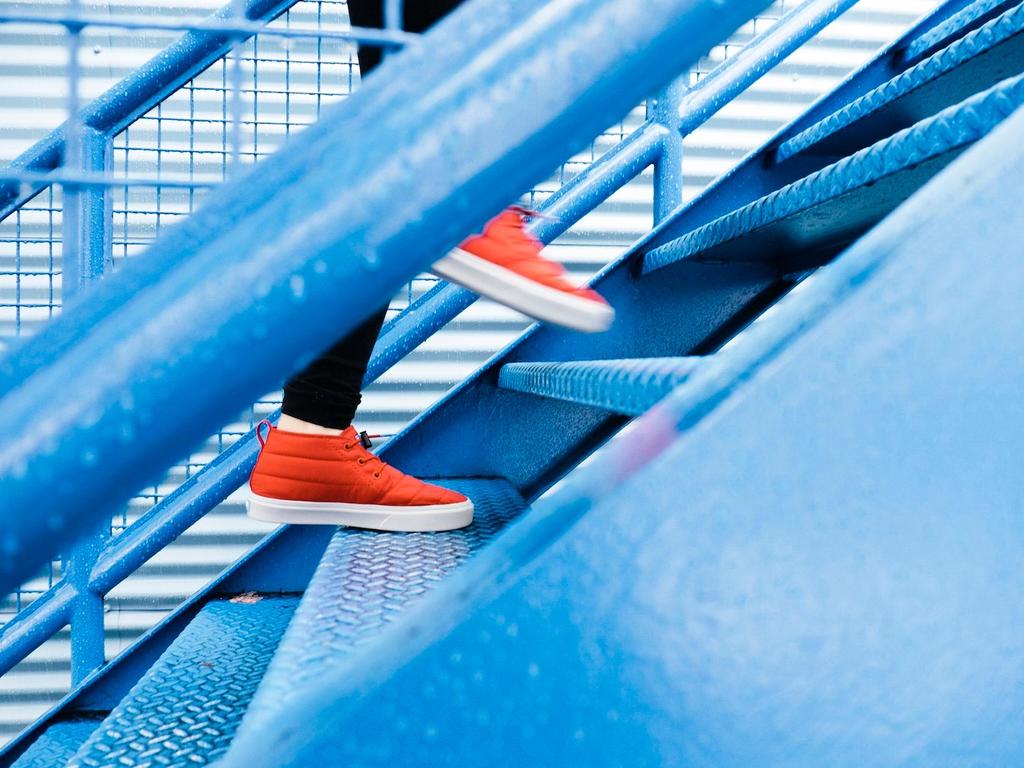 A person walking up blue metal stairs wearing bright red shoes.