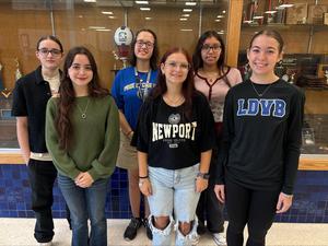A group of six students smiling in front of a trophy case