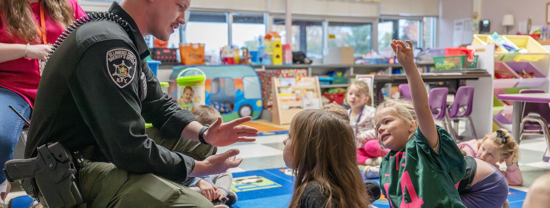 School resource officer kneeling to speak with preschool students