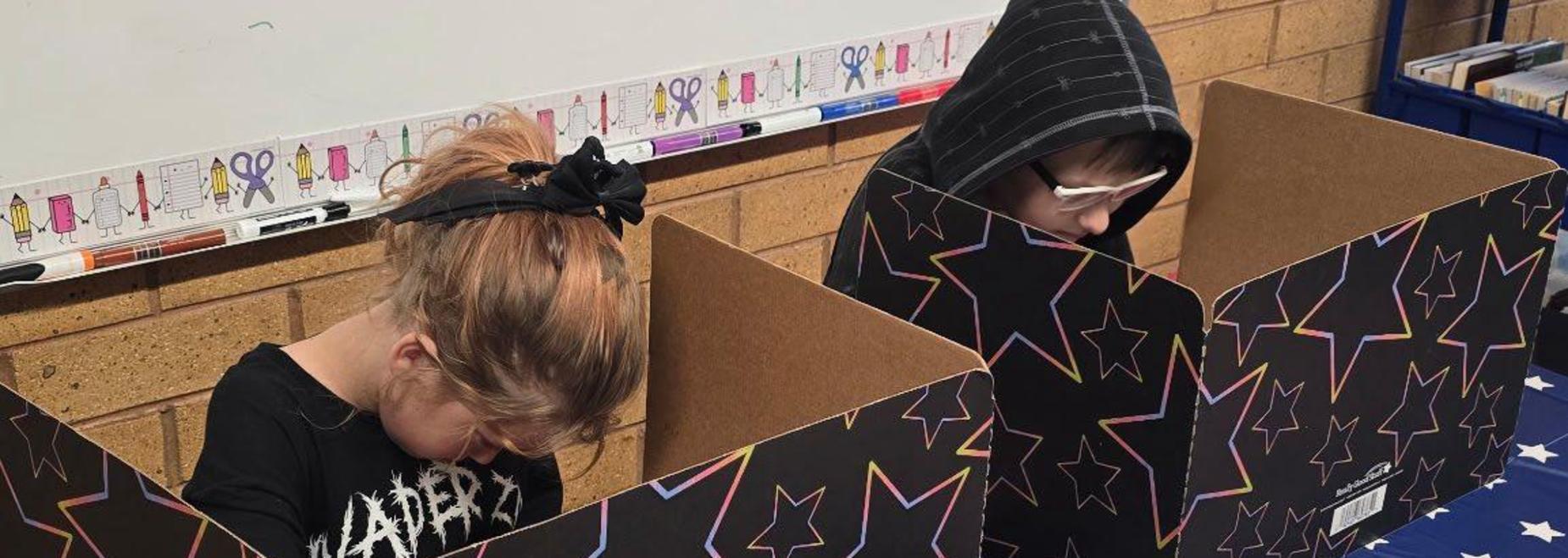 Two children focused on their work at desks with colorful dividers.