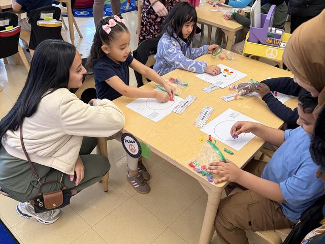 Children and adults engaged in a craft activity at a classroom table.