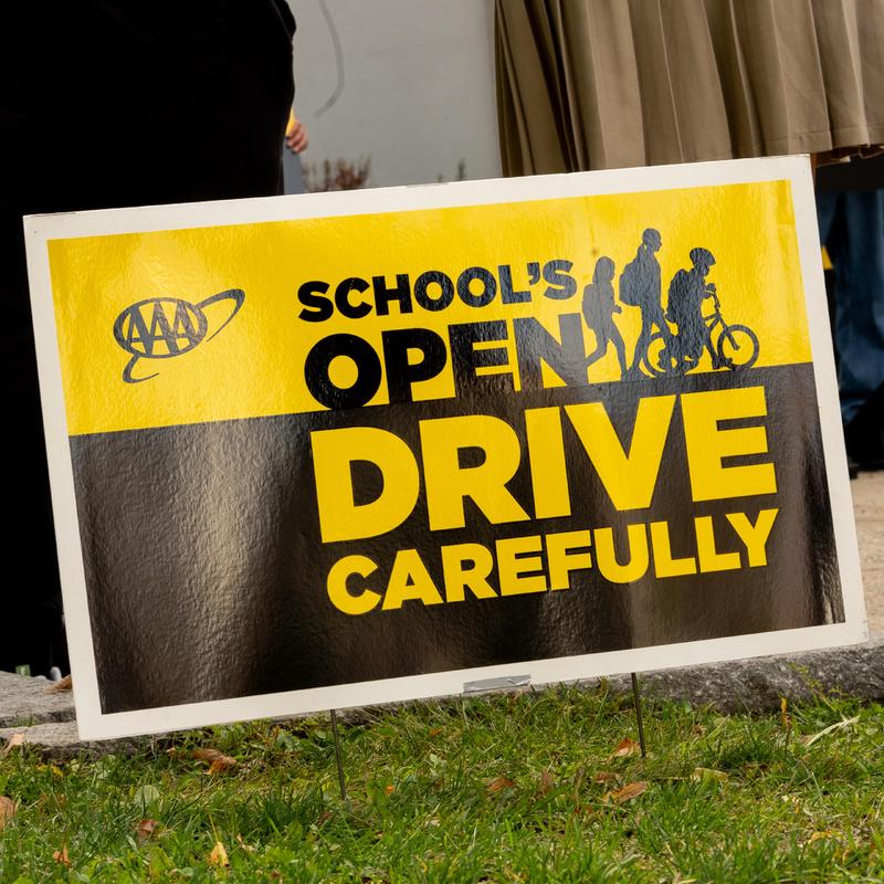 Sign promoting cautious driving near an open school zone with children walking and biking.