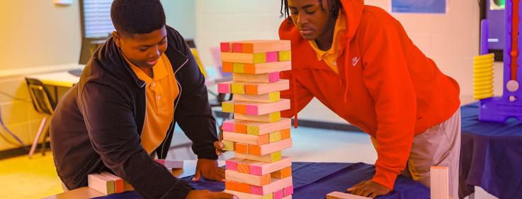 Two young men playing a game with colorful stacked blocks.