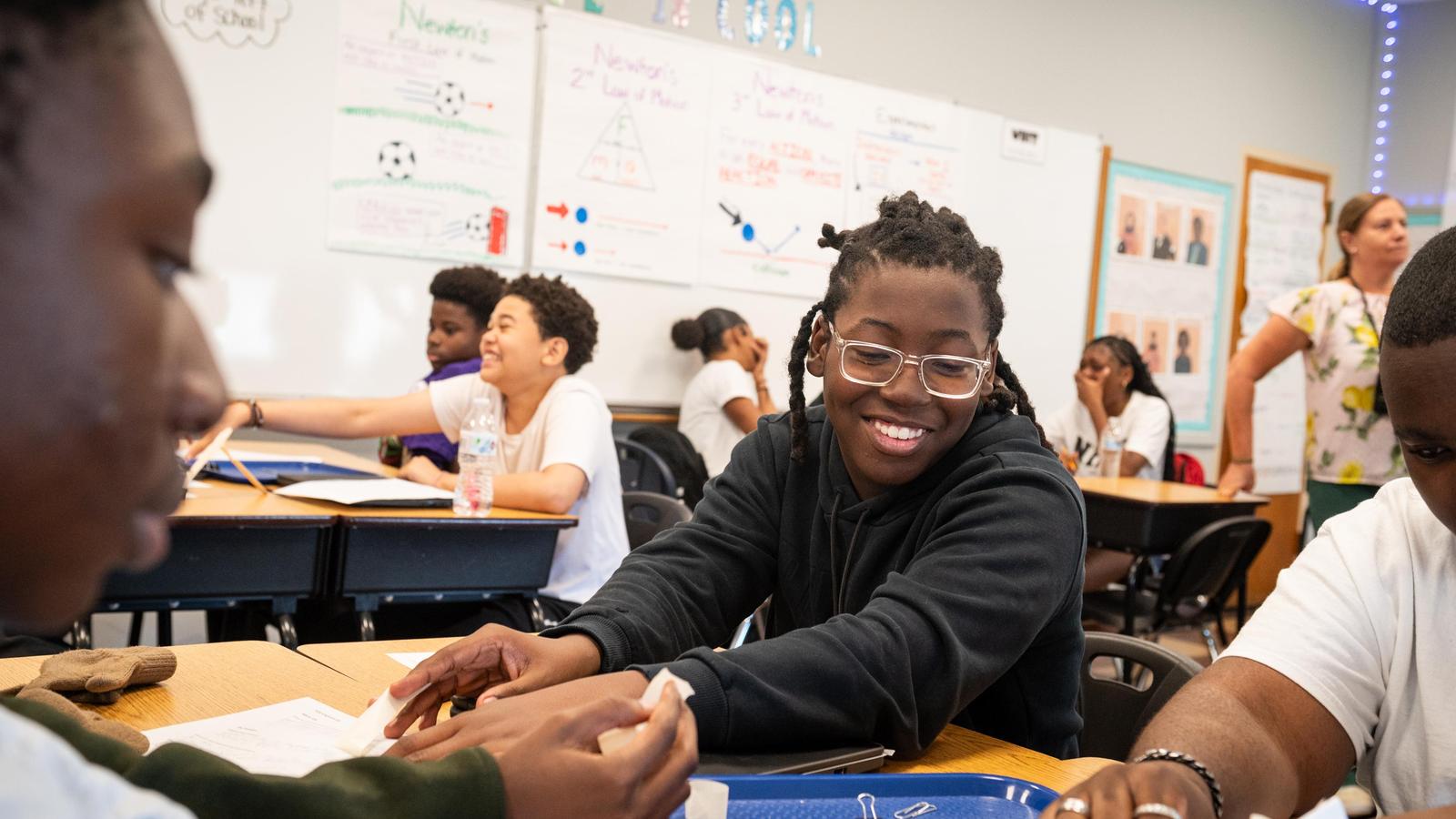 Student smiling while reaching across desk