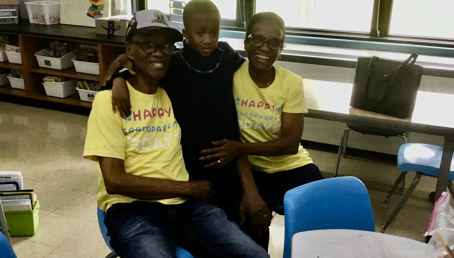 A boy in a dark shirt is hugged by two adults in yellow shirts at a school event.