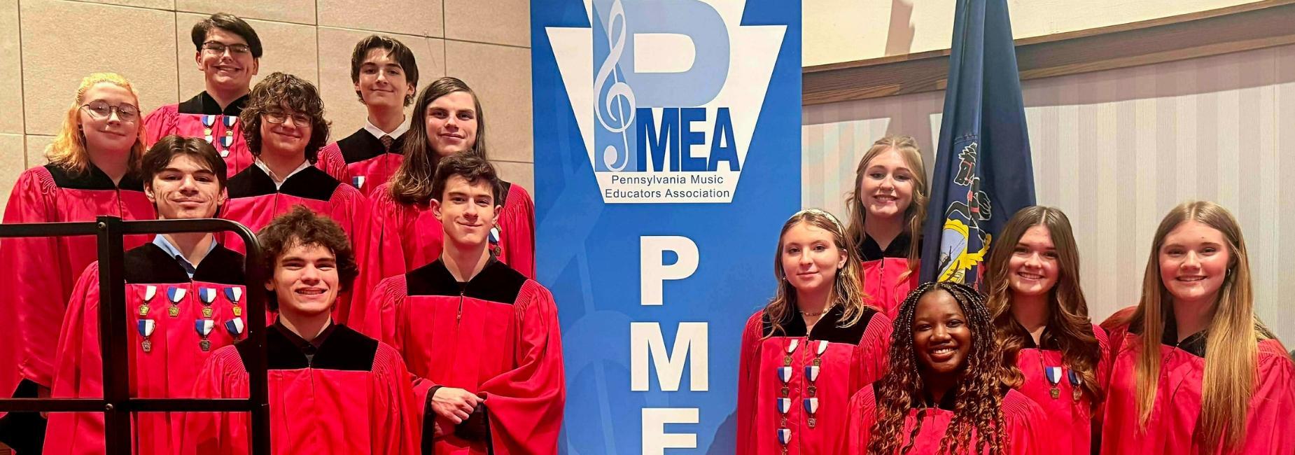 Group of students in red robes with a PMEA banner.