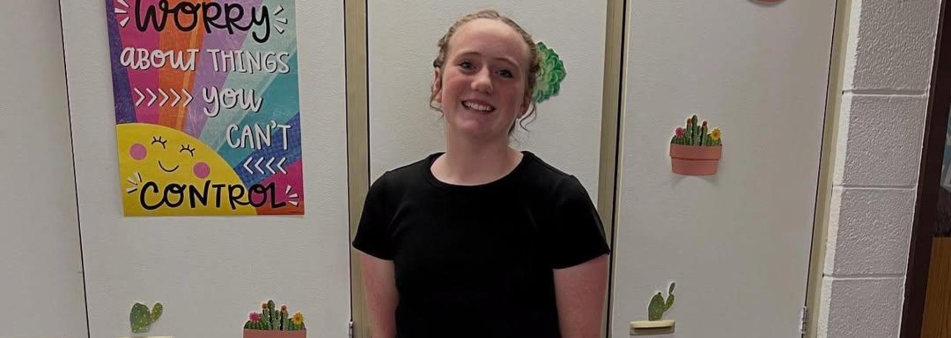 A person in a black top and jeans standing in front of decorated school lockers.