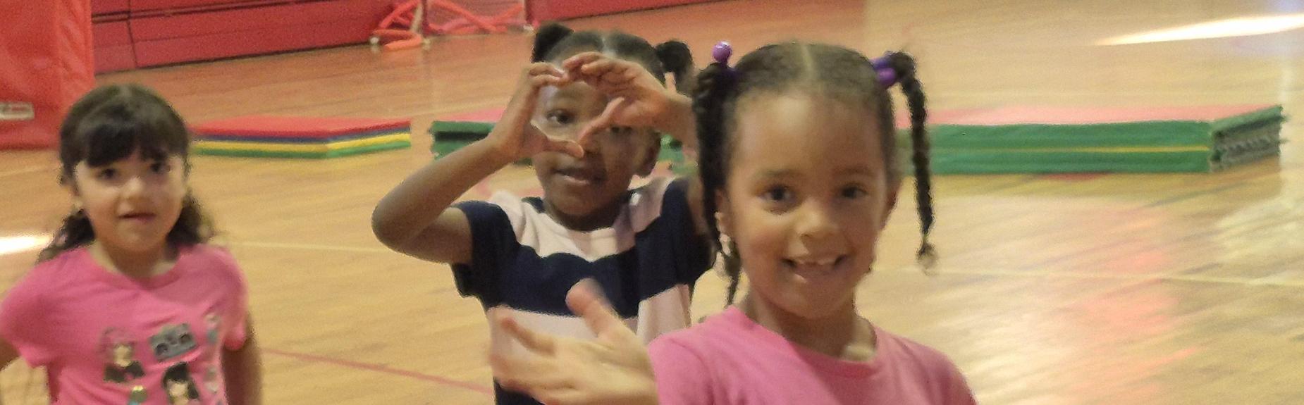 Group of children smiling and waving in a gymnasium setting.