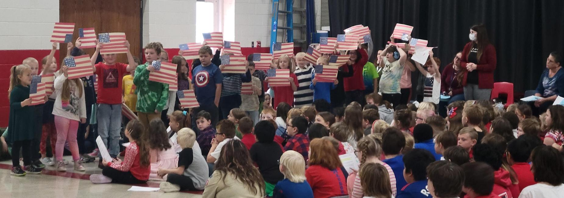 1st grade students at Atkins Elementary holding flags during a Veteran's Day assembly on 11/11/2022.