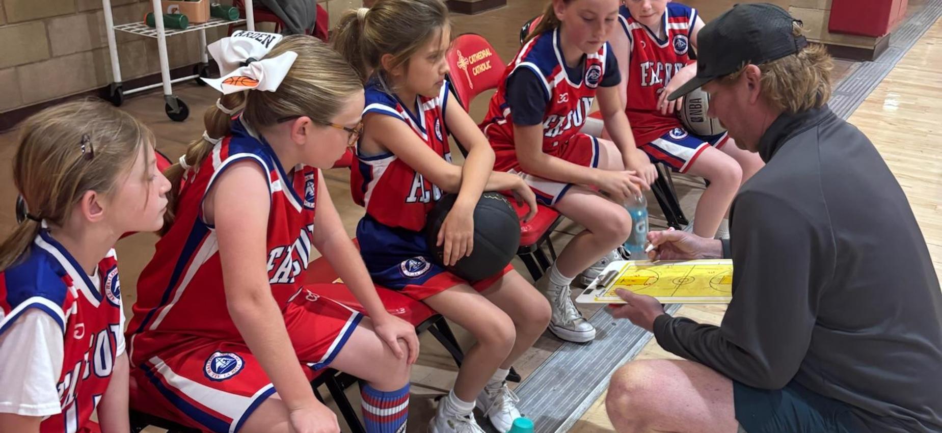 3rd/4th grade girls basketball team listens to coach on sideline during a timeout