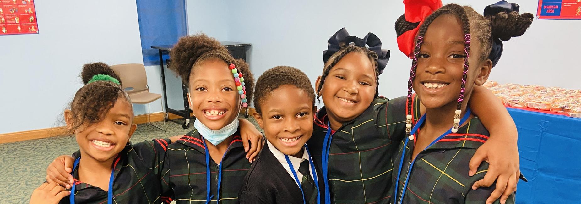 Six children smiling together, wearing matching plaid uniforms and ID badges.