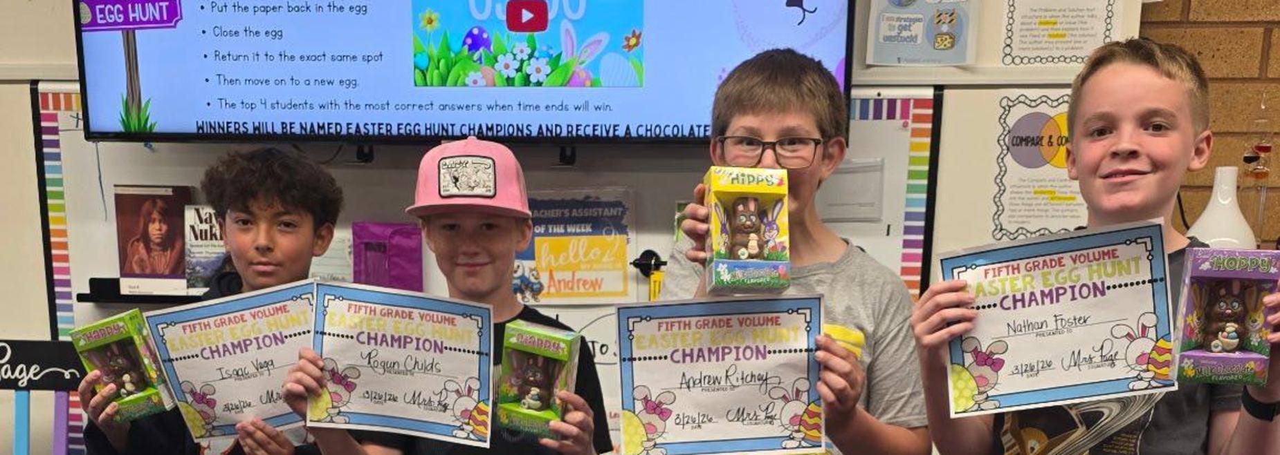 Four kids hold certificates in a classroom setting.