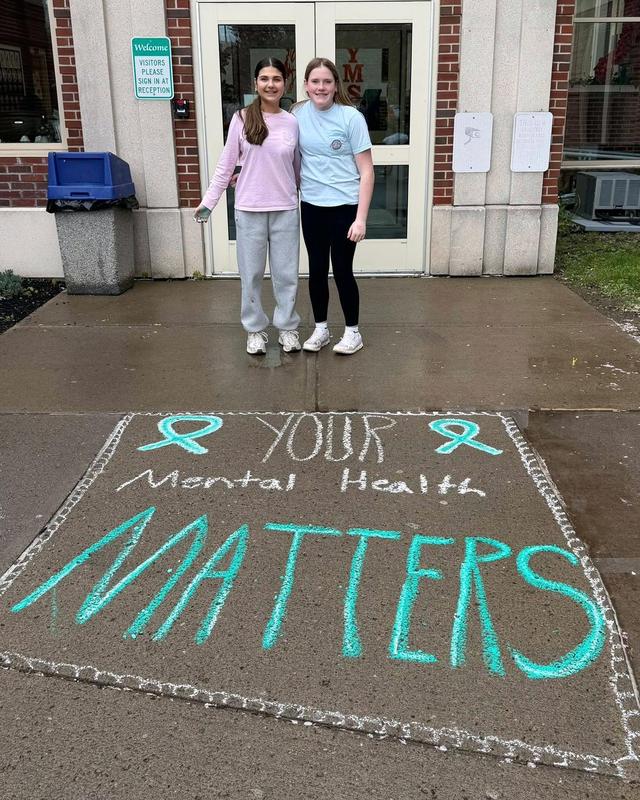 Students smile behind a green chalk drawing of the words 