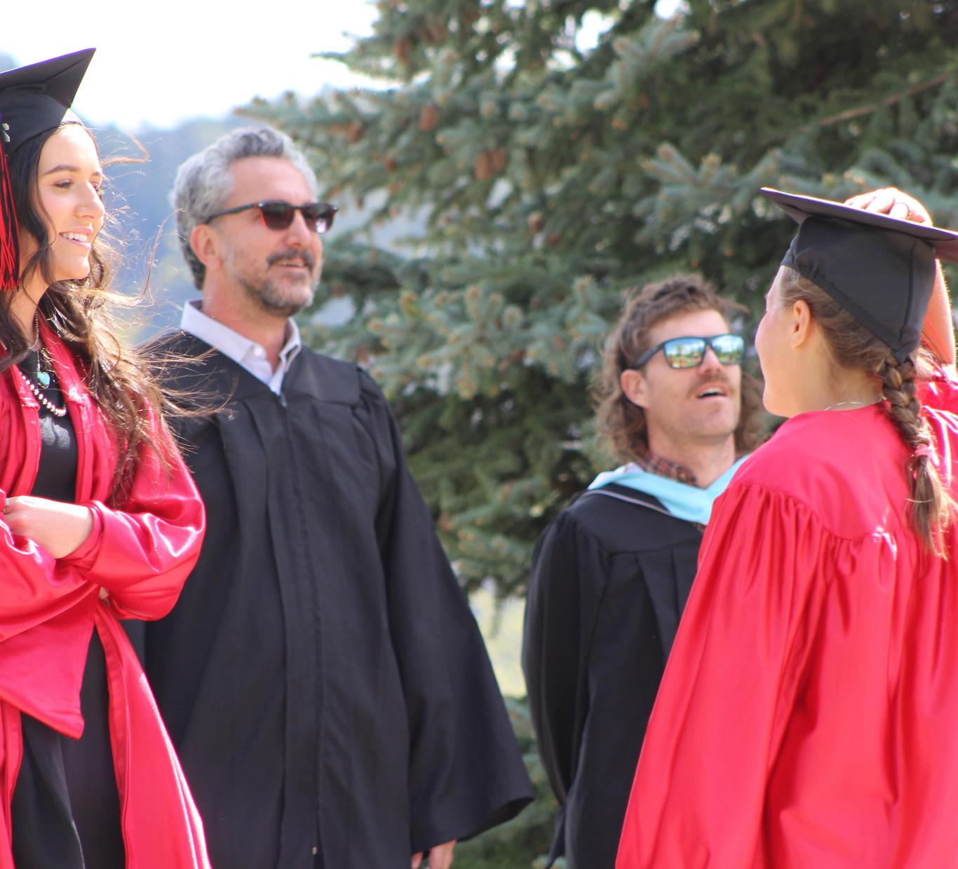 Graduating students in red gowns pose with smiling adults outdoors.