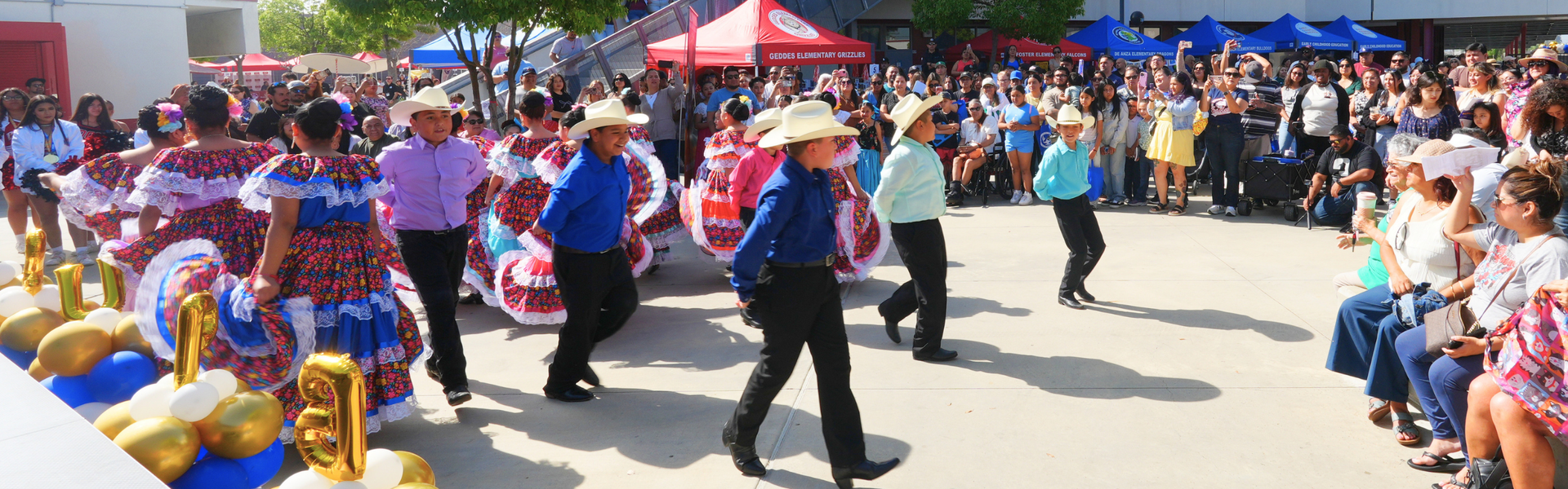 Dancers in traditional attire perform for a large audience at an outdoor event.