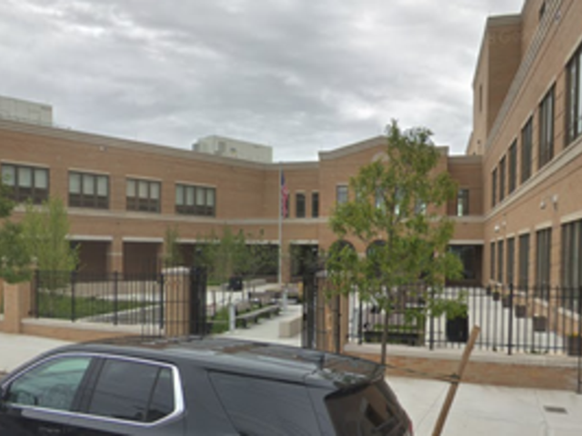A school building with an outdoor courtyard and trees, surrounded by a fence.
