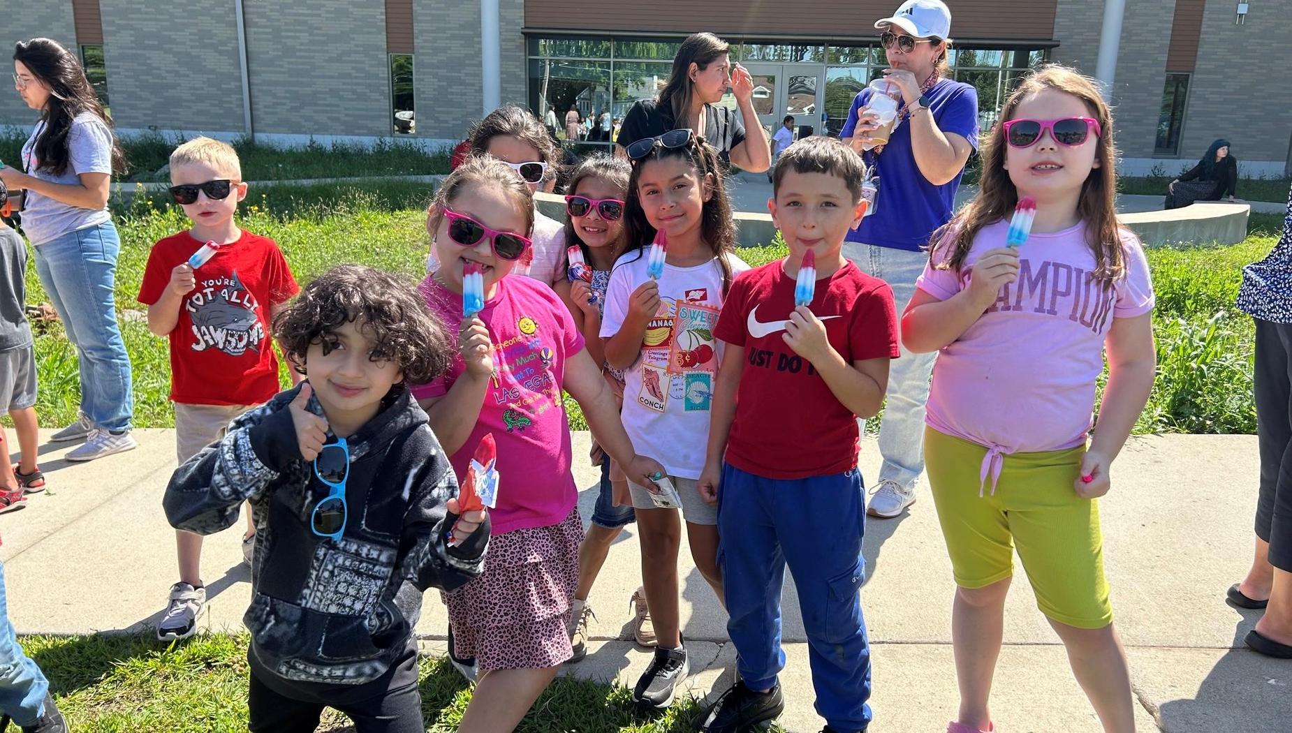 Children wearing sunglasses and ice pops posing outdoors.