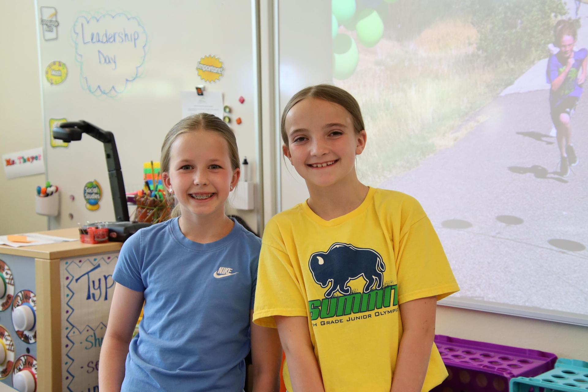 two elementary school girls smiling for the camera in a classroom
