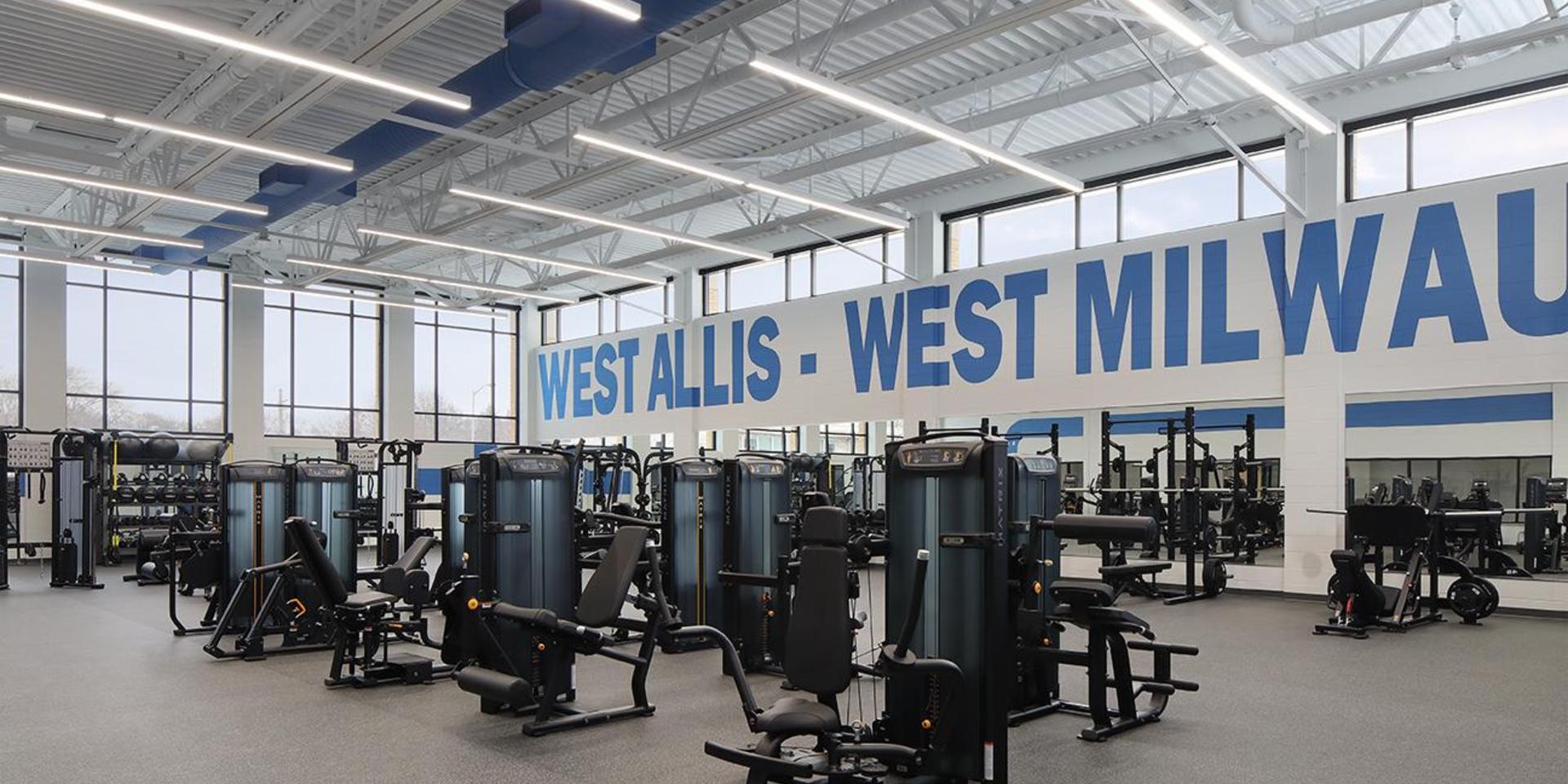 A bright gym with exercise machines and a large wall sign.