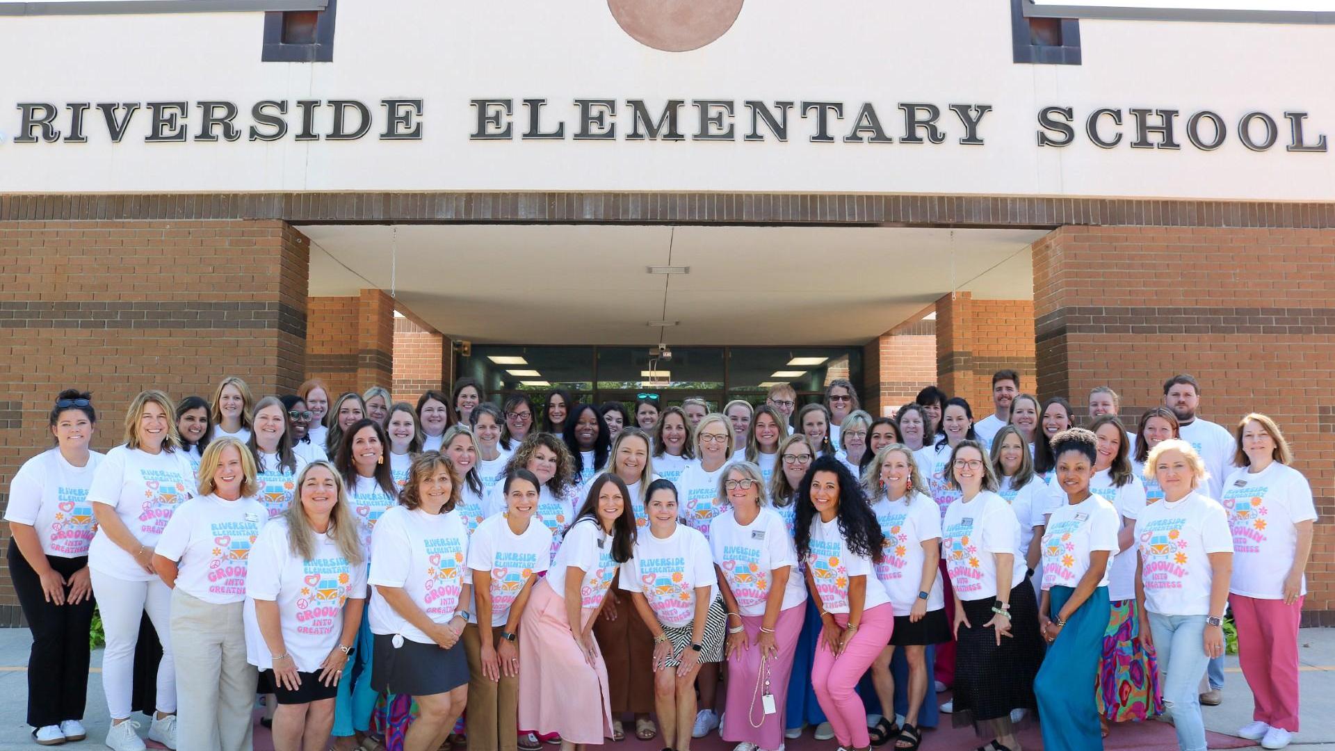 Group photo of faculty and staff outside Riverside Elementary School, all wearing matching t-shirts.