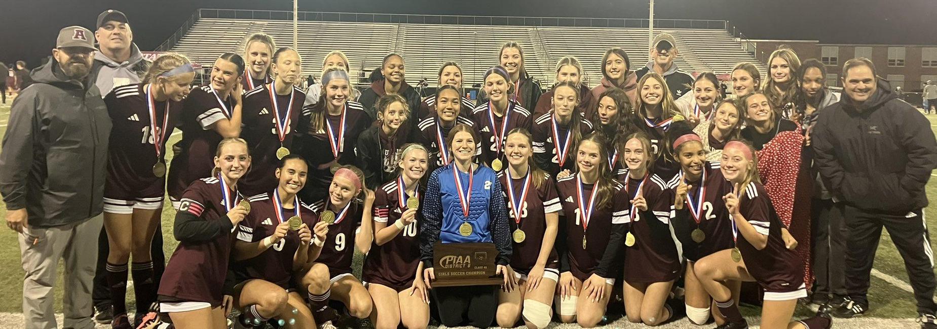 Soccer team celebrating with medals and a trophy under stadium lights.