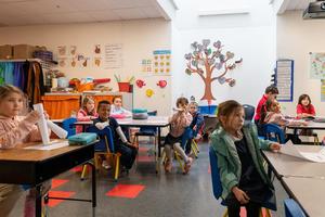 Students in a brightly colored classroom at Arco Iris Spanish Immersion School sit at desks. They are facing a speaker who is out of the image.