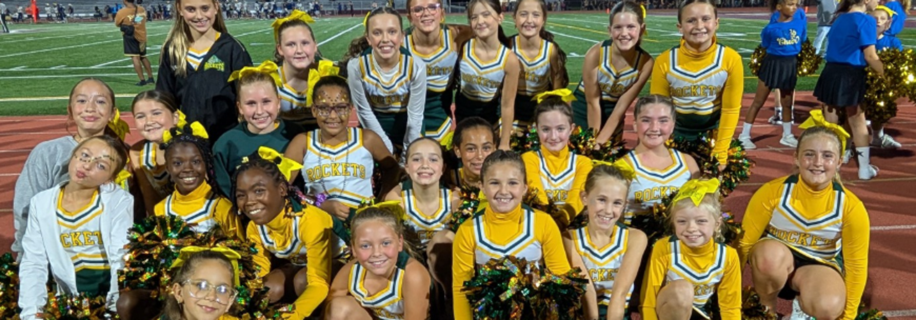 Cheerleaders in uniforms pose together with pom-poms on a sports field.