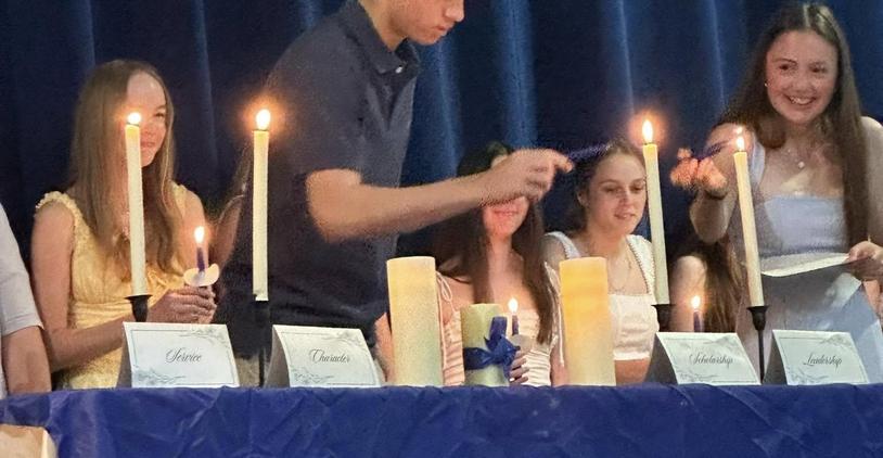 Students lighting candles at a ceremony table with awards and decorations.