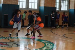 Teens playing basketball in a gym with a vibrant wooden court.