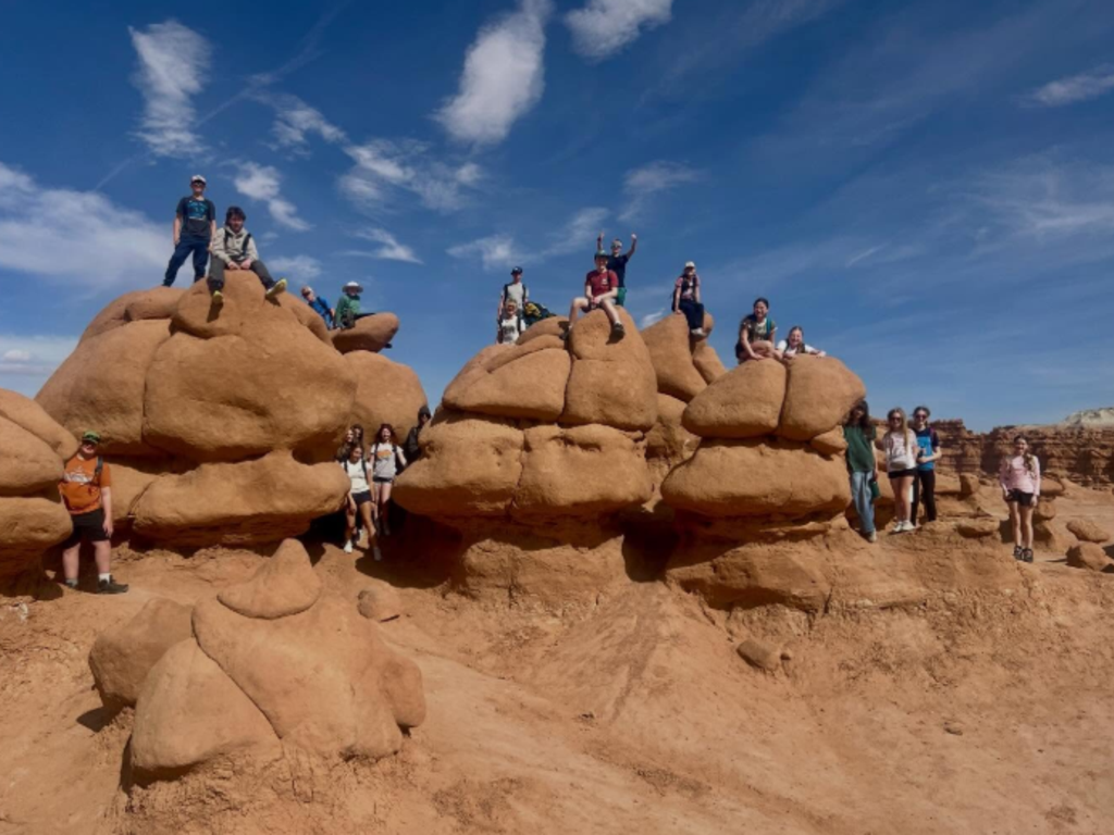 Students sitting on top of large, red rocks in the desert.
