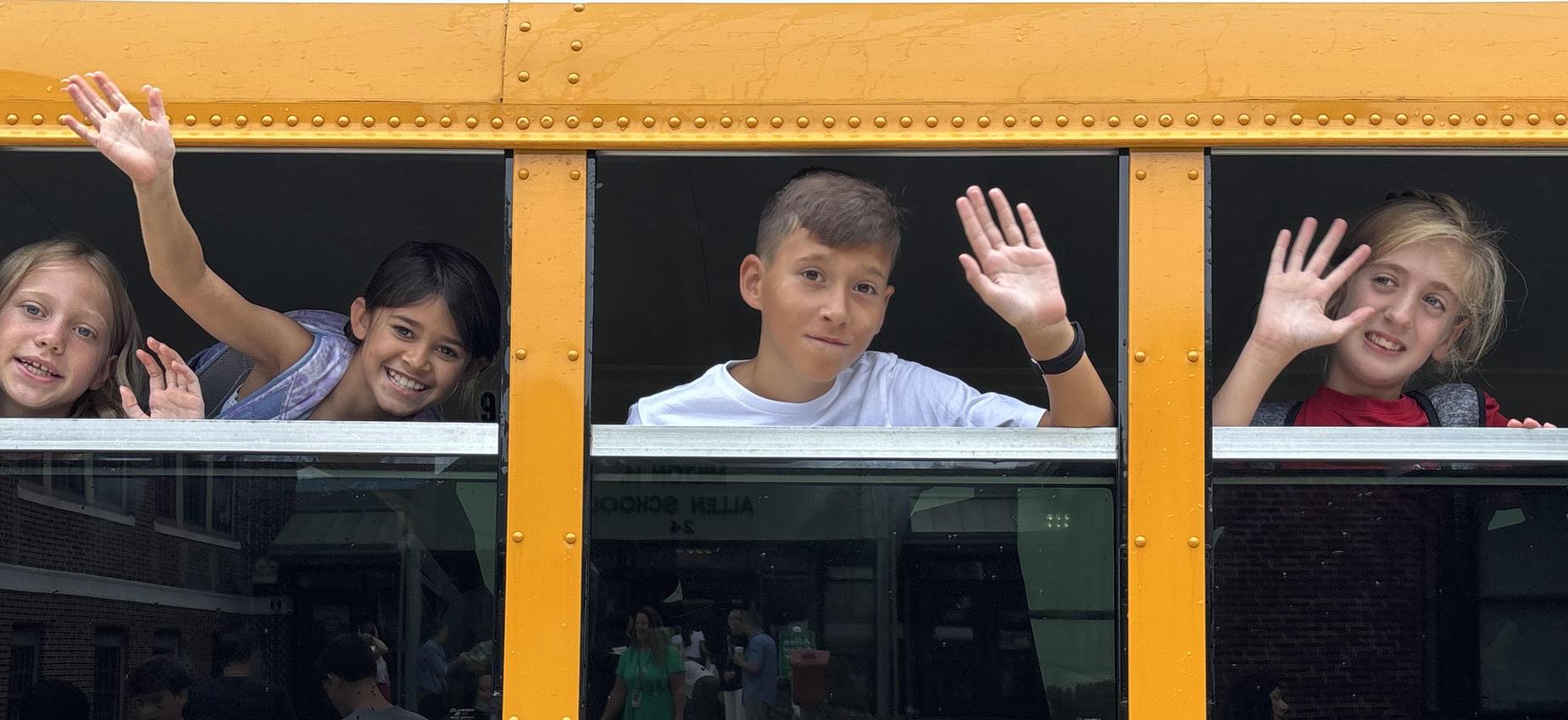 Children waving from a school bus window with smiles.