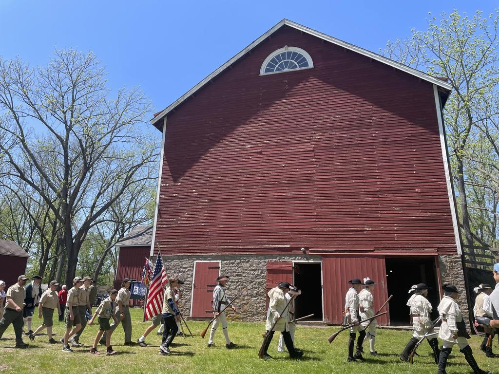 A group of students in historic costume walking in front of a red bank barn at Tinicum Park for the Upper Bucks 250 Heritage Day event.