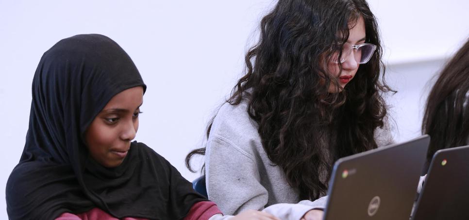 Two students working on laptops, one in a hijab and the other with curly hair.