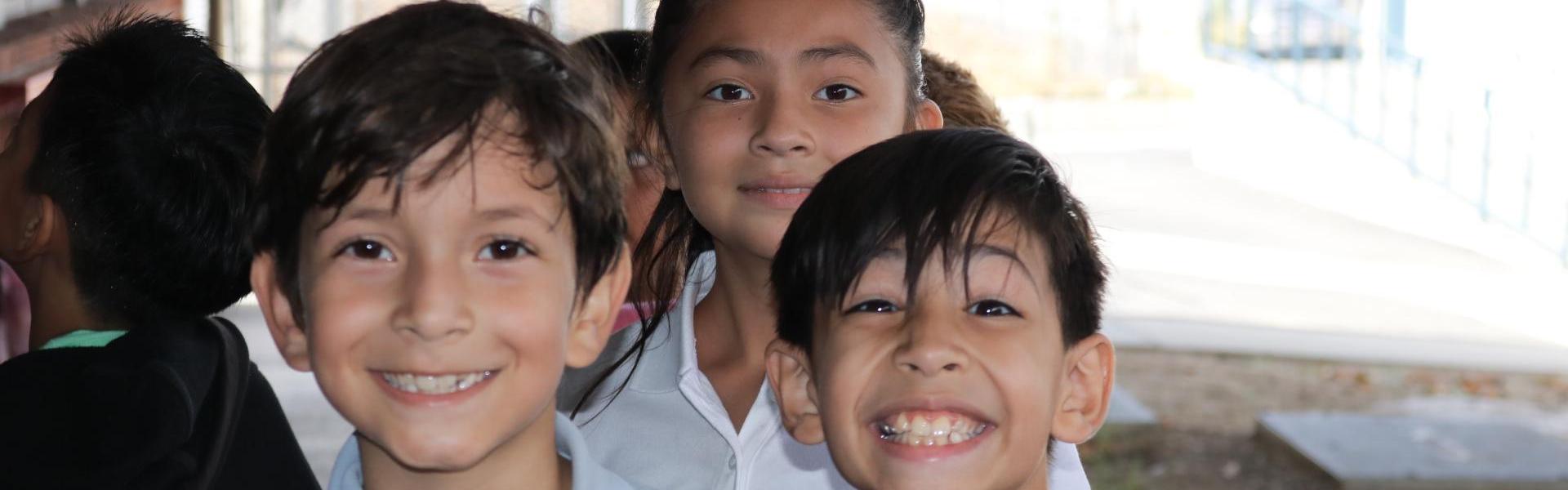 Three smiling children posing together outdoors.