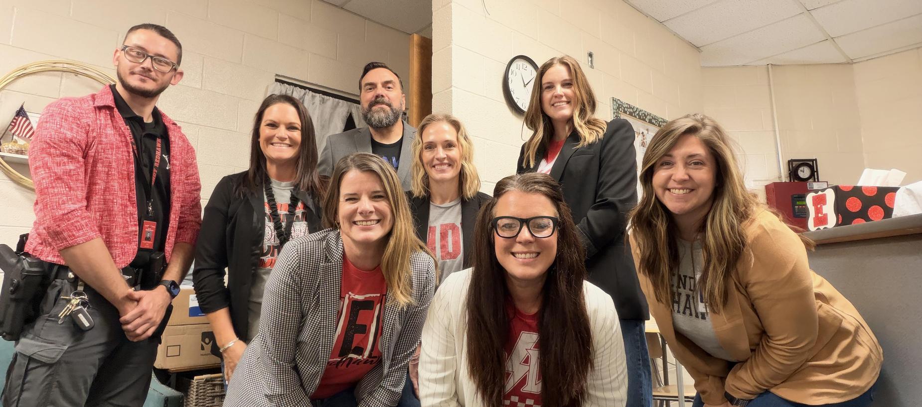 A group of nine smiling educators posing together in a classroom setting.