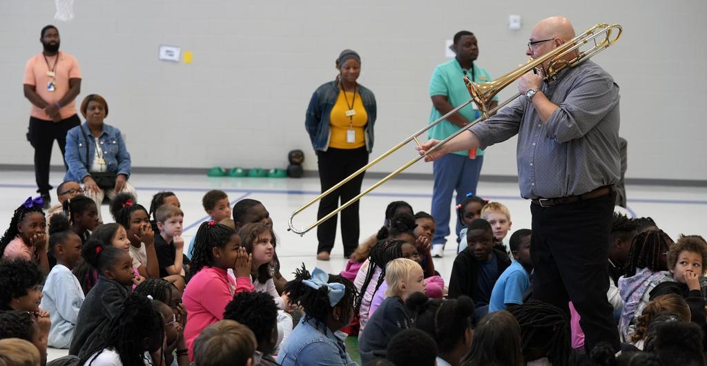 A trombonist plays music while surrounded by students