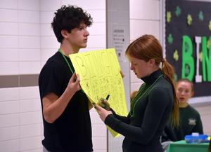 a girl crossing off numbers on a yellow poster held by a boy
