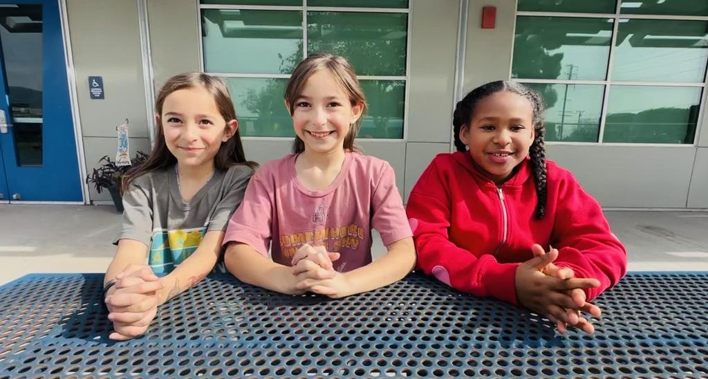 Three girls sitting together at a table, smiling.