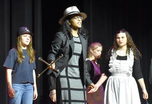 Students acting on stage in various costumes during a performance.