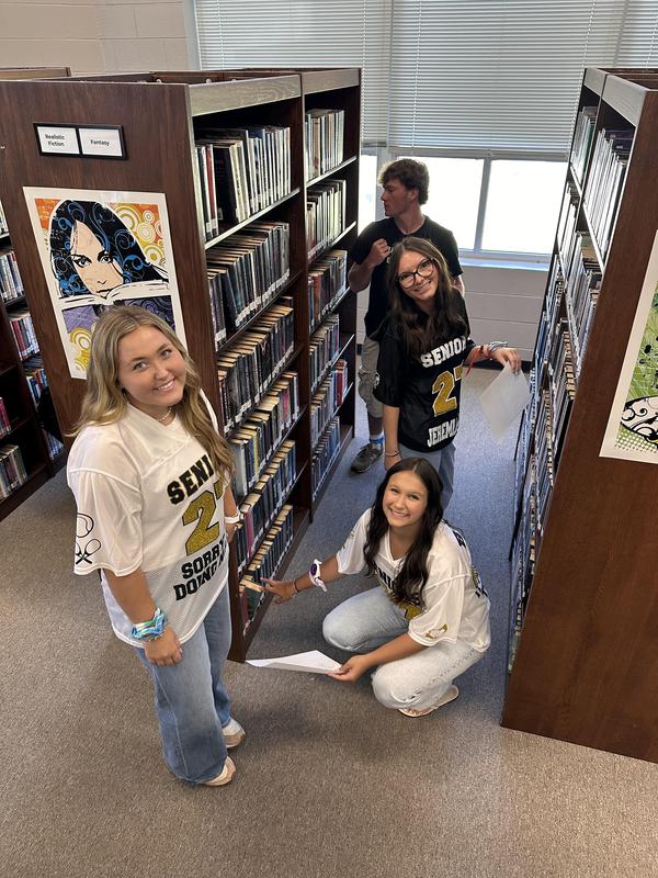 Four students pose while looking for a library book