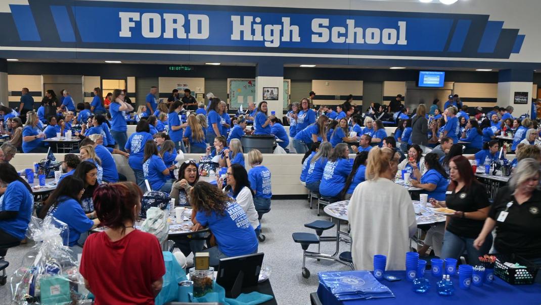 A crowded school cafeteria filled with people in blue shirts engaging in activities.
