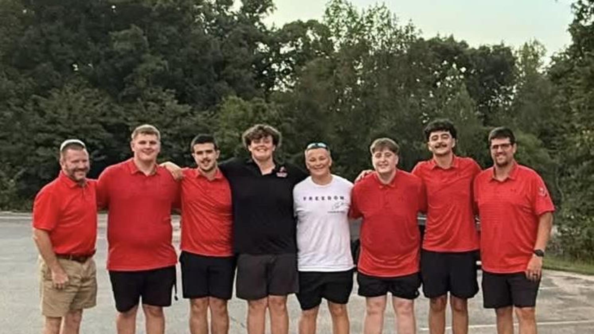 A group of young men in red shirts posing together outdoors.