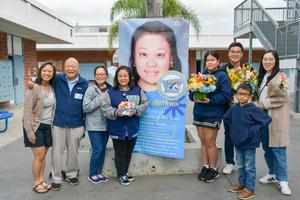 Rebecca Chai stands with her family, smiling next to her Teacher of the Year banner.