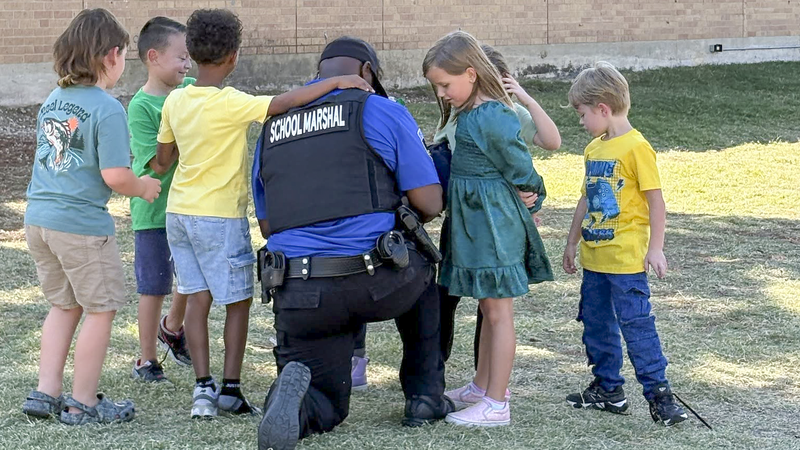 School marshal in uniform kneeling and helping tie a student's shoe