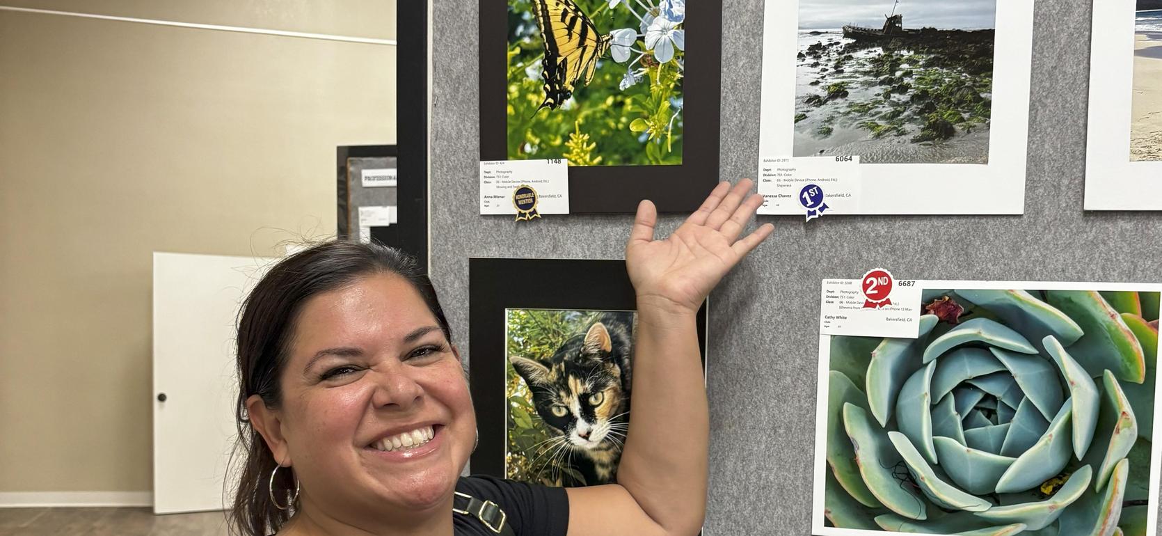 Smiling woman holds a photo of a cat next to various framed images on display.